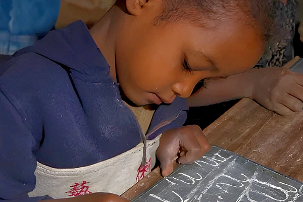 Young boy writes on a chalkboard, highlighting learning and educational opportunity.