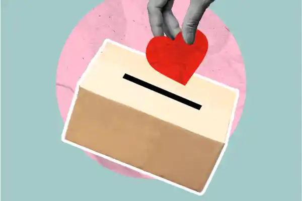 Hand places a heart into a donation box to represent charitable giving and outreach.